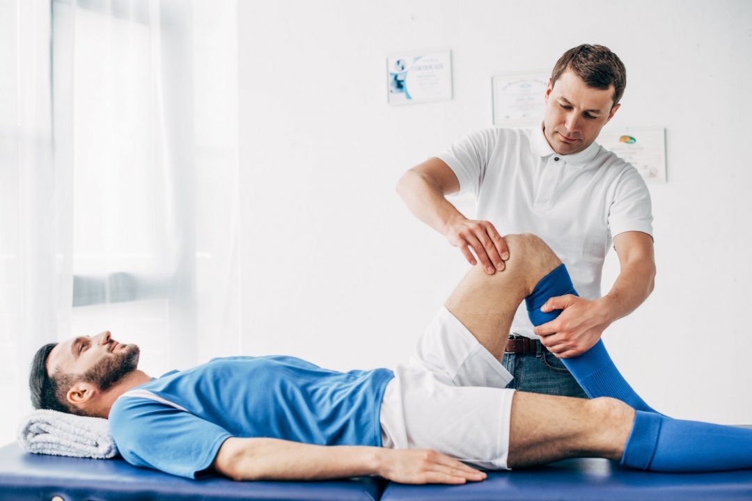 Handsome physiotherapist massaging leg of football player in hospital - lighthouse chiropractic | family chiropractic center | fort collins, co | experienced practitioner professionals | fort collins chiropractic care & massage therapy